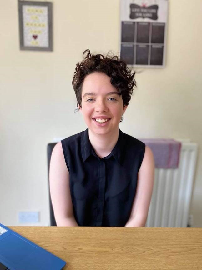 Hollie sat on a chair, behind a table, smiling