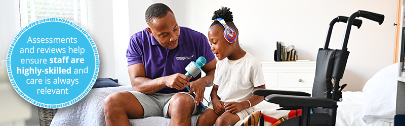 Image of young boy being supported by a healthcare assistant to do something he enjoys. He is singing into a microphone while sat on the edge of the bed. At the side of him is his wheelchair. To the left is a blue roundal with white text that reads, "Assessments and reviews help ensure staff are highly-skilled and care is always relevant."