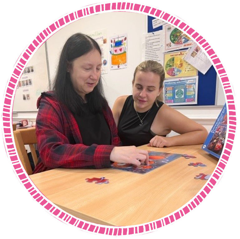 A picture of Wendy, a person we support, with her support worker. They are doing a jigsaw puzzle at the dining room table. 