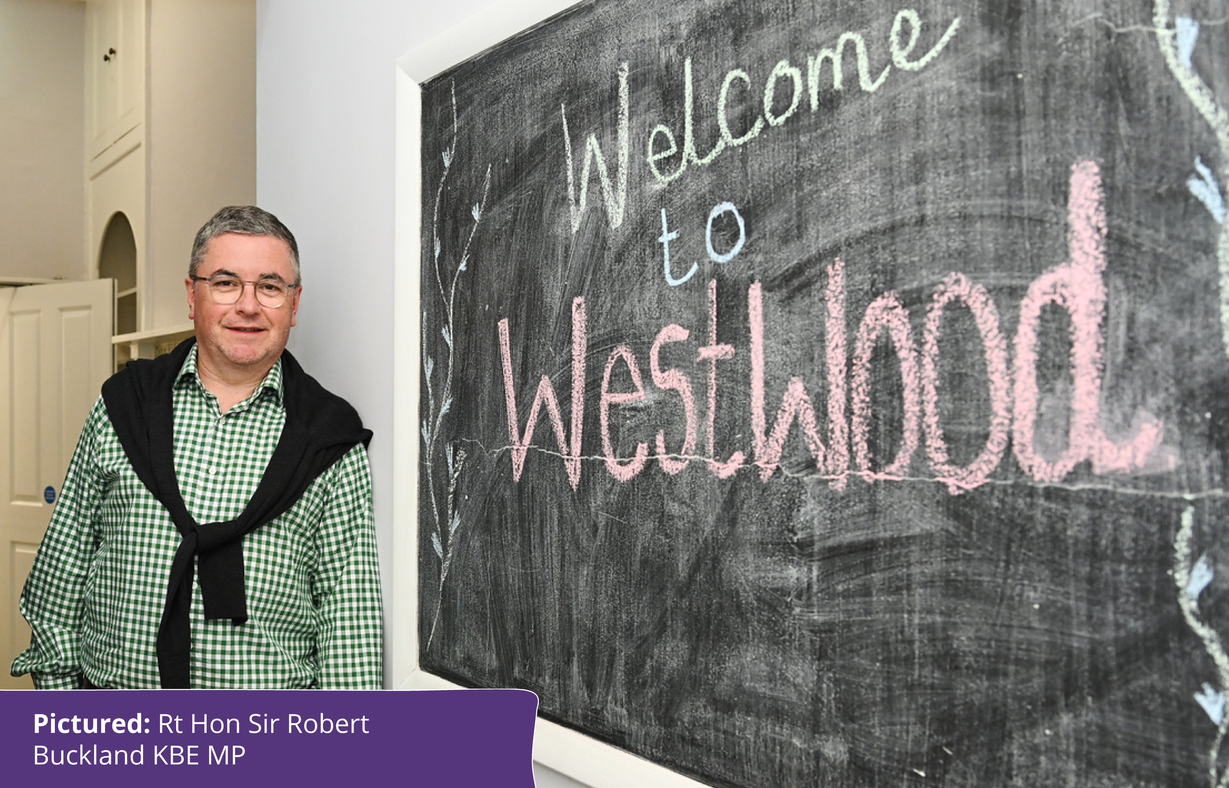 Rt Hon Sir Robert Buckland KBE MP next to welcome to Westwood sign.